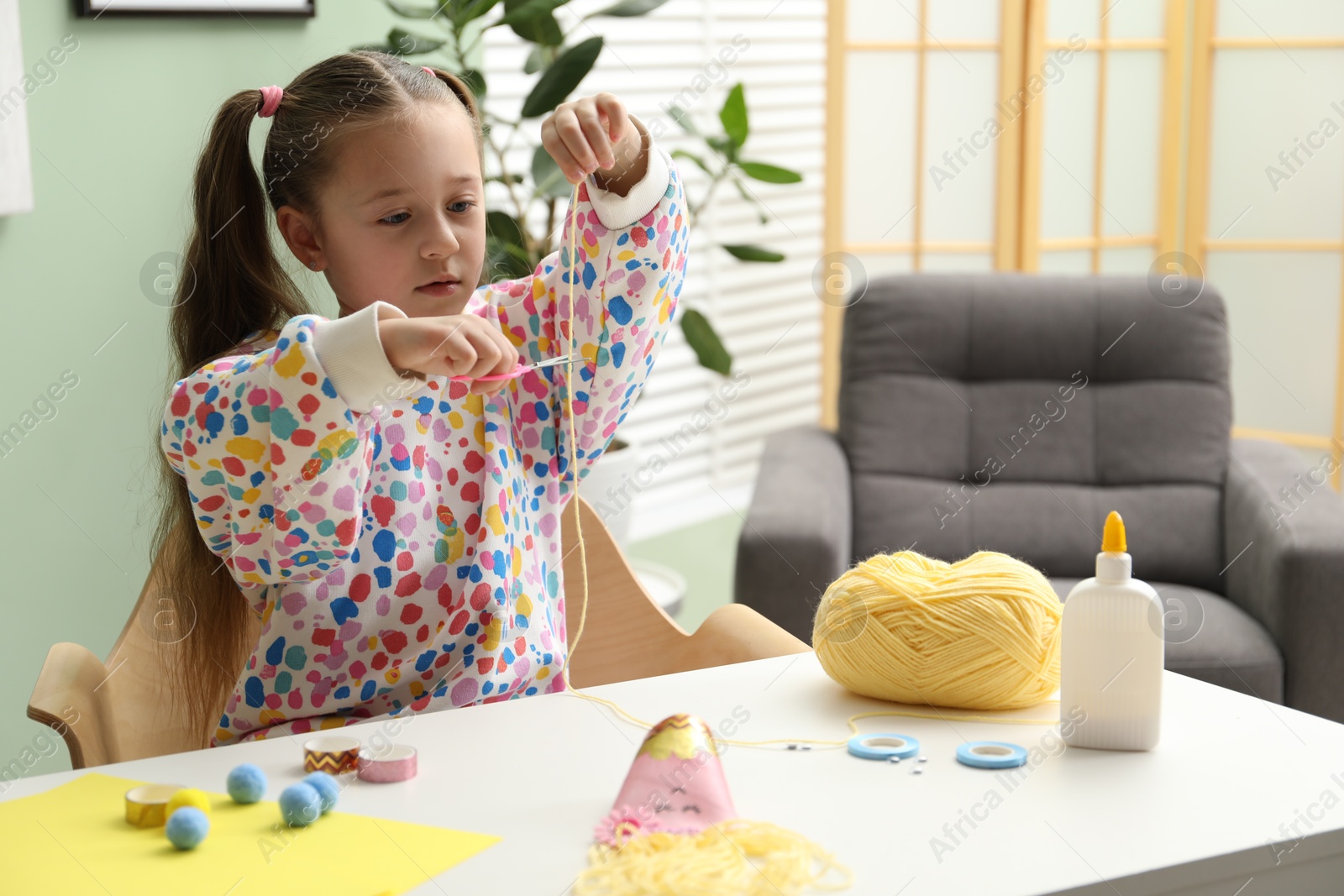 Photo of Little girl making craft at white table indoors. Child creativity