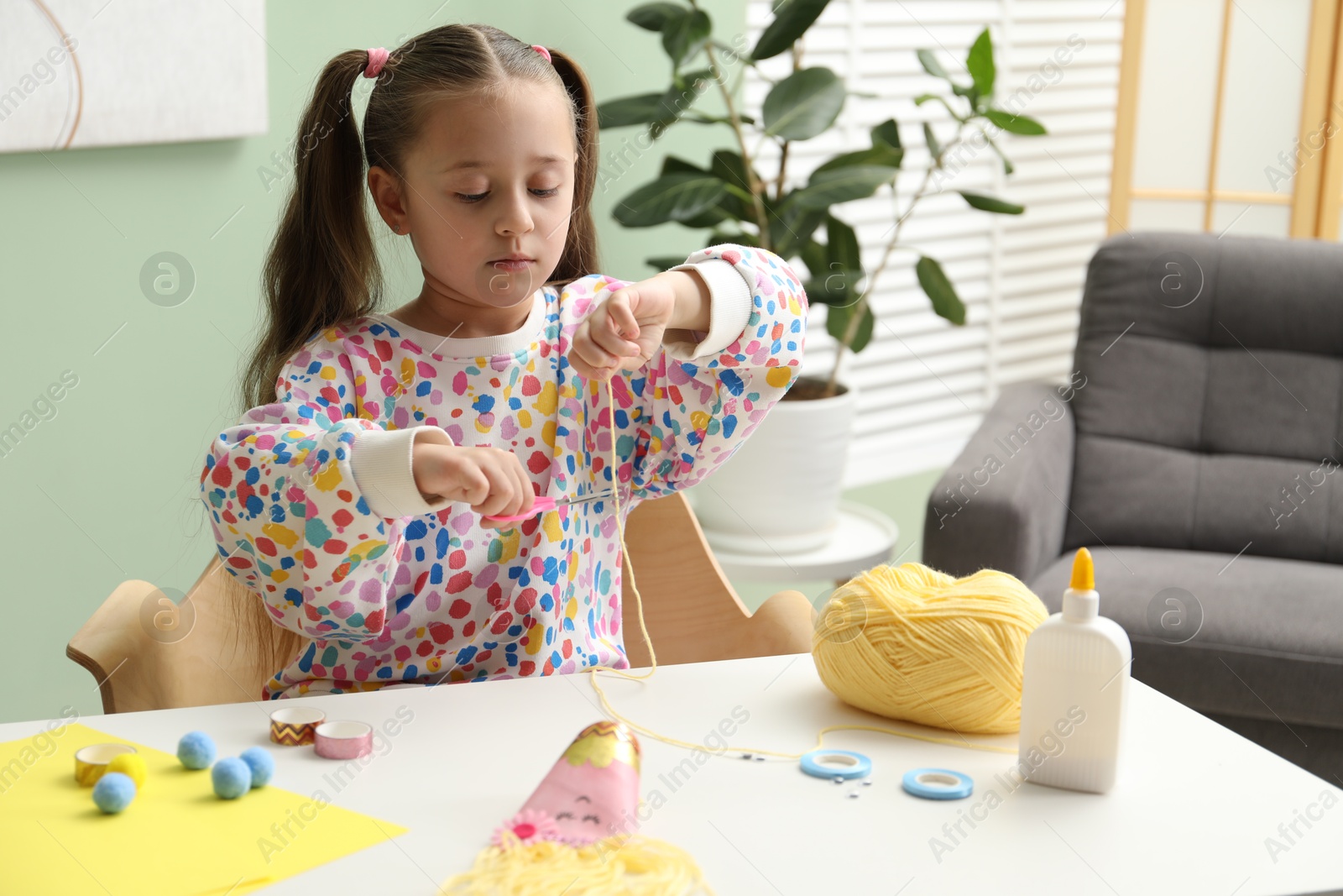 Photo of Little girl making craft at white table indoors. Child creativity