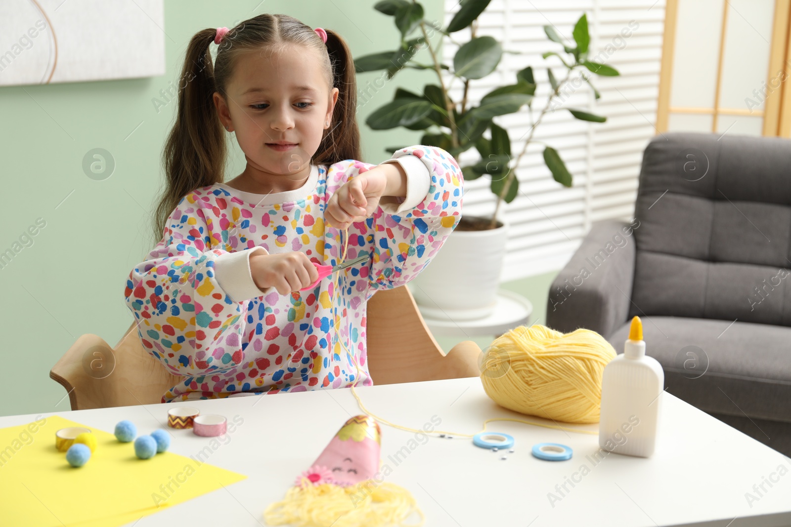 Photo of Little girl making craft at white table indoors. Child creativity