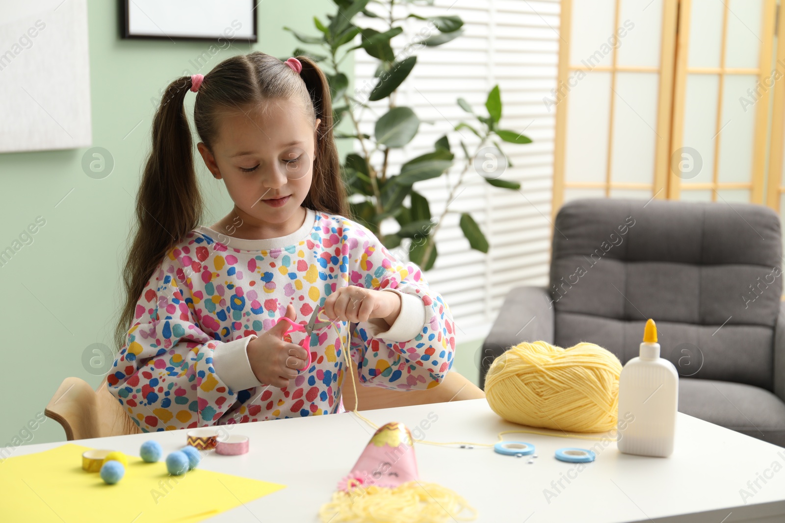 Photo of Little girl making craft at white table indoors. Child creativity