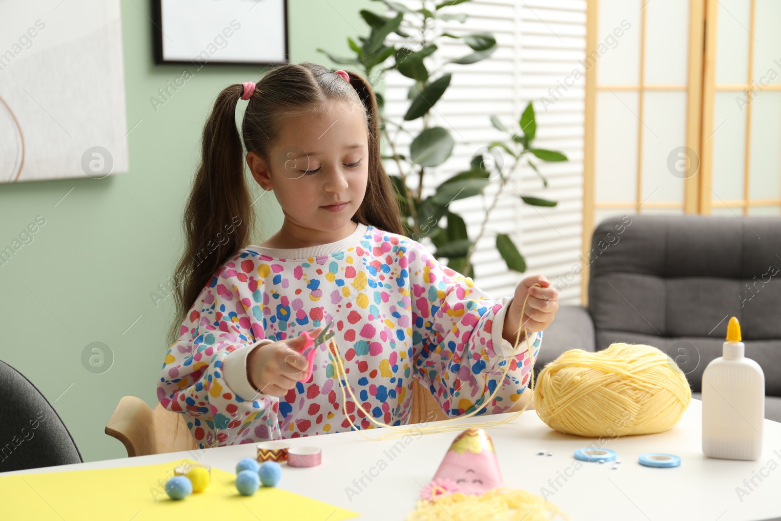 Photo of Little girl making craft at white table indoors. Child creativity