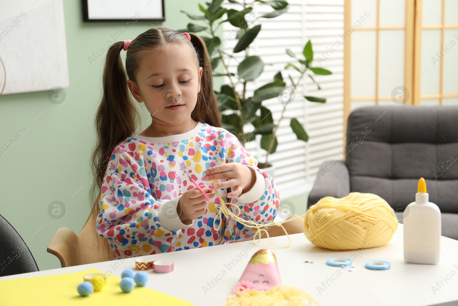 Photo of Little girl making craft at white table indoors. Child creativity