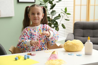 Photo of Little girl making craft at white table indoors. Child creativity