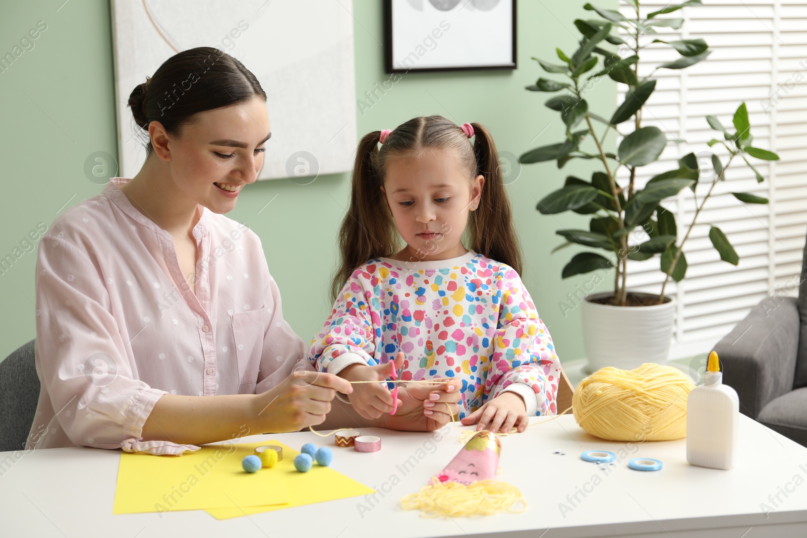 Photo of Woman and little girl making craft at white table indoors. Child creativity