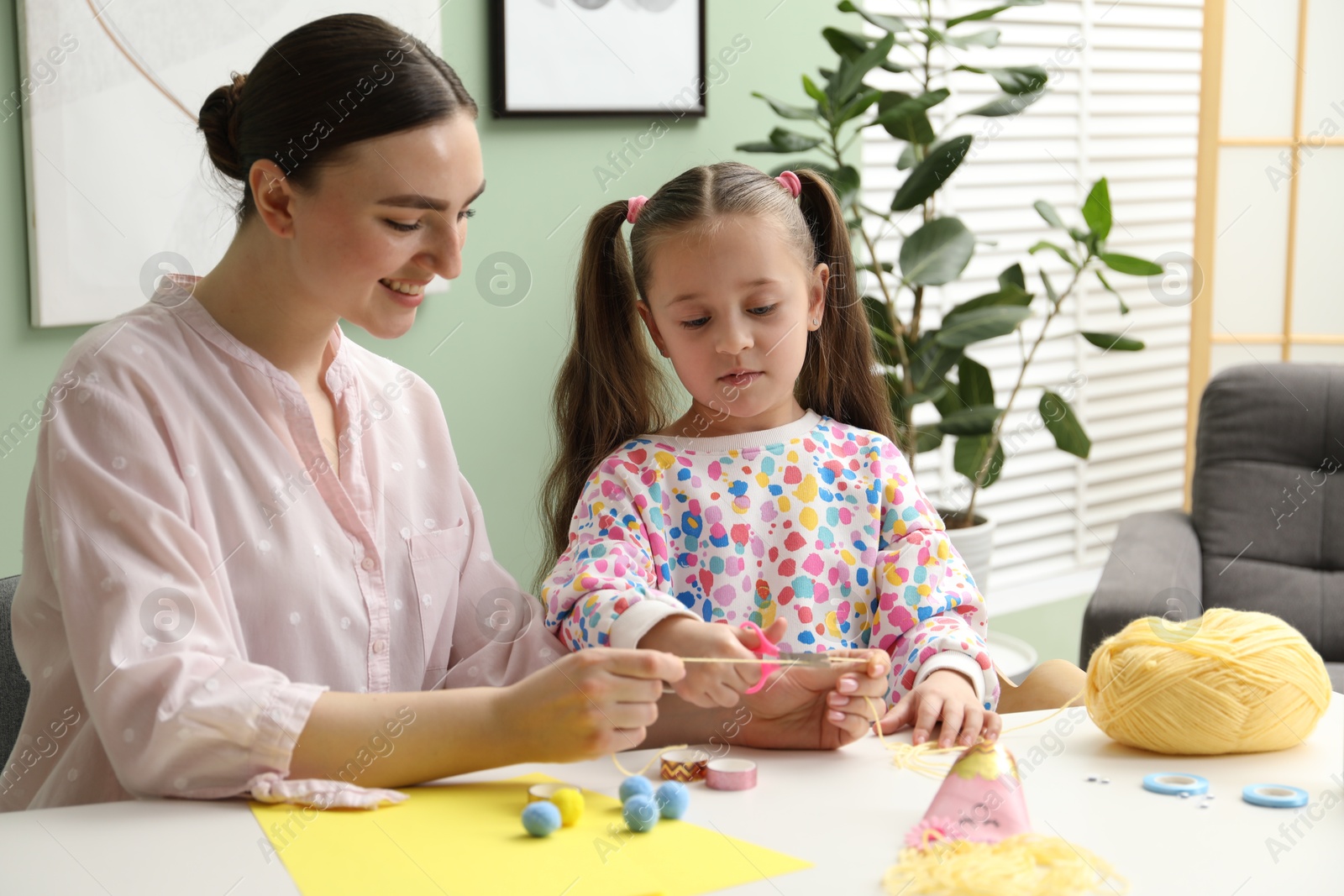 Photo of Woman and little girl making craft at white table indoors. Child creativity