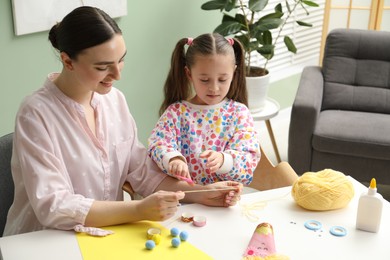 Woman and little girl making craft at white table indoors. Child creativity