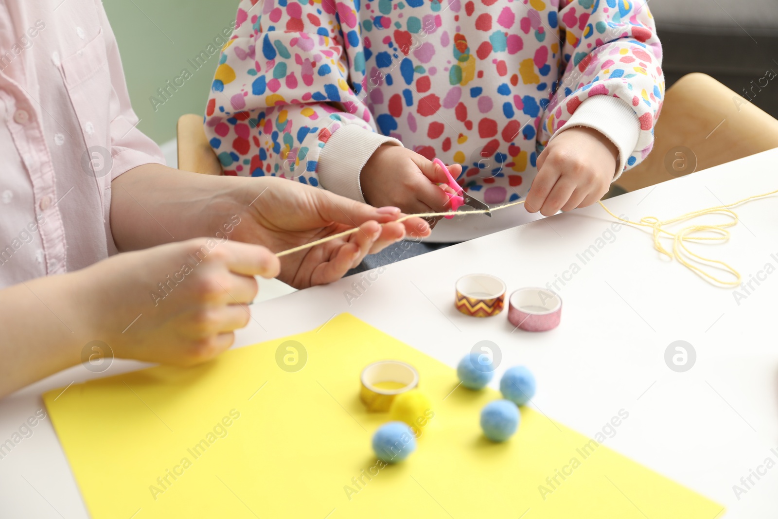 Photo of Woman and little girl making craft at white table indoors, closeup. Child creativity