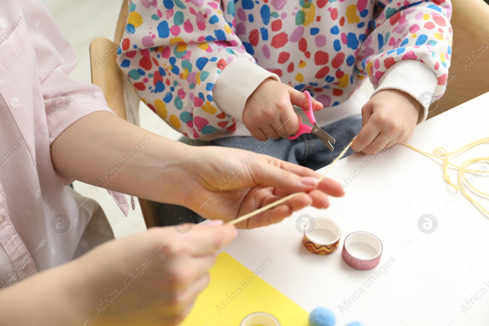 Photo of Woman and little girl making craft at white table indoors, closeup. Child creativity