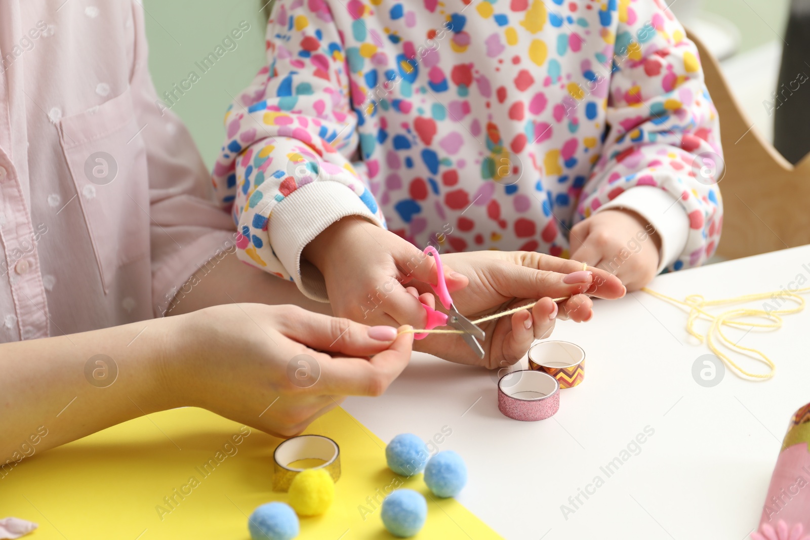 Photo of Woman and little girl making craft at white table indoors, closeup. Child creativity