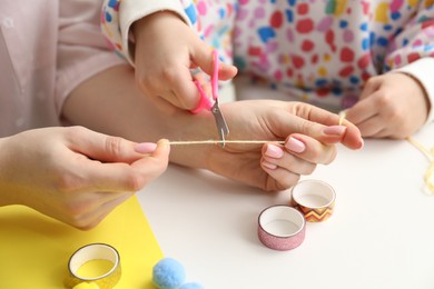 Photo of Woman and little girl making craft at white table indoors, closeup. Child creativity