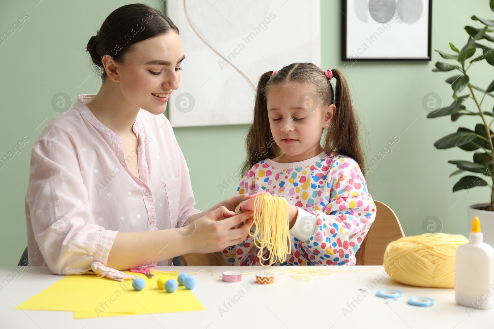 Photo of Woman and little girl making craft at white table indoors. Child creativity