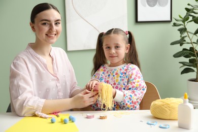 Woman and little girl making craft at white table indoors. Child creativity