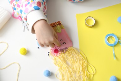 Photo of Little girl with handmade toy at white table, top view. Child creativity and craft