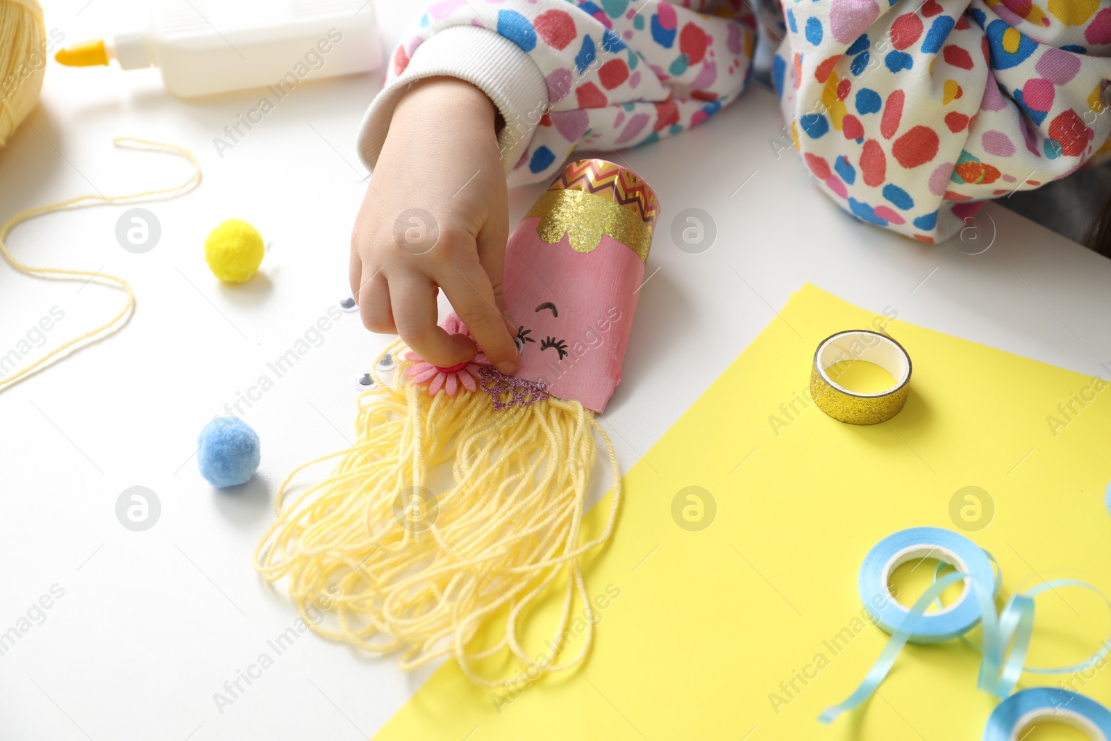 Photo of Little girl with handmade toy at white table, closeup. Child creativity and craft