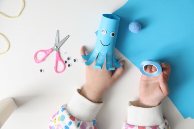 Photo of Little girl with handmade octopus at white table, top view. Child creativity and craft