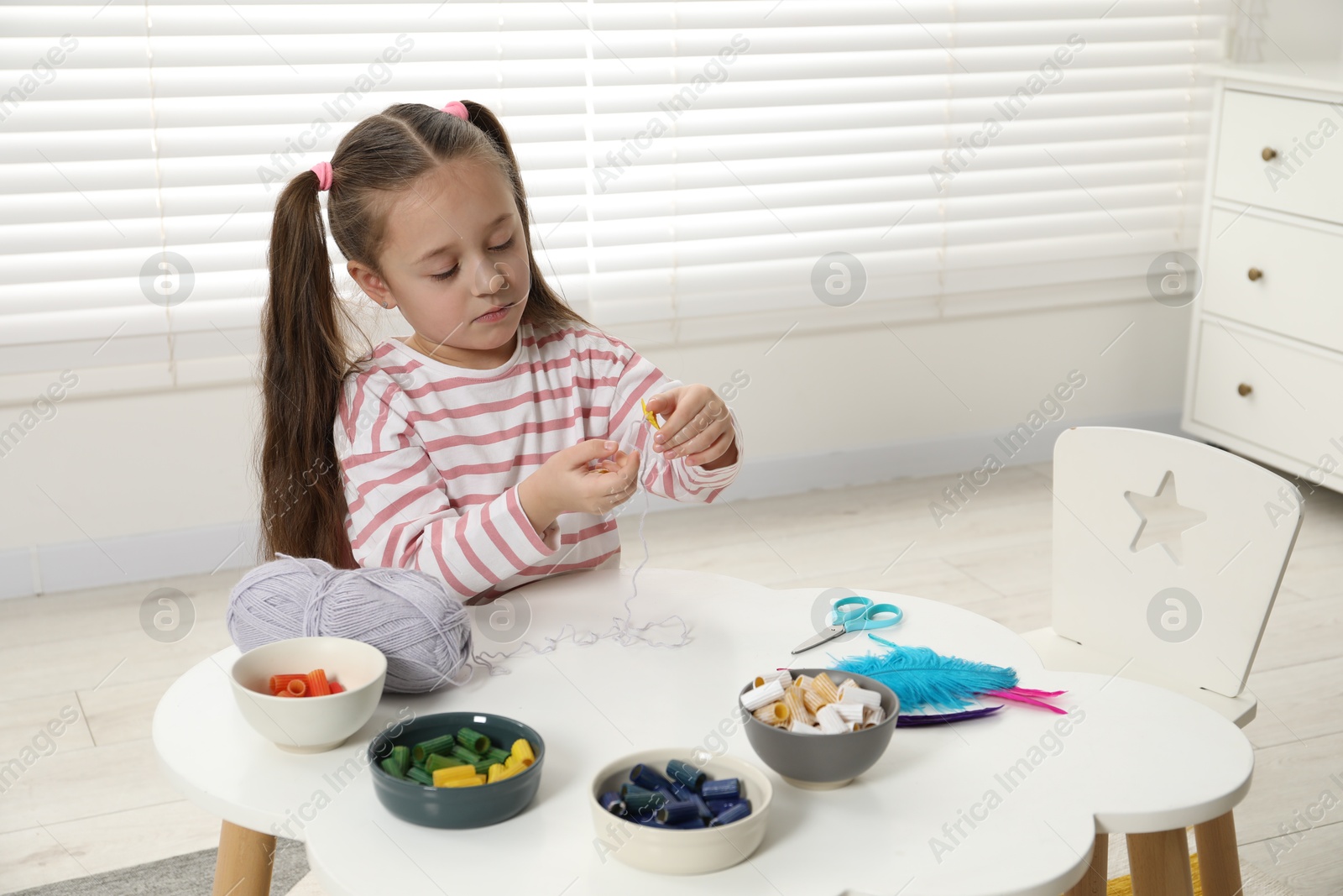 Photo of Little girl making craft at white table indoors. Child creativity and handmade handicraft