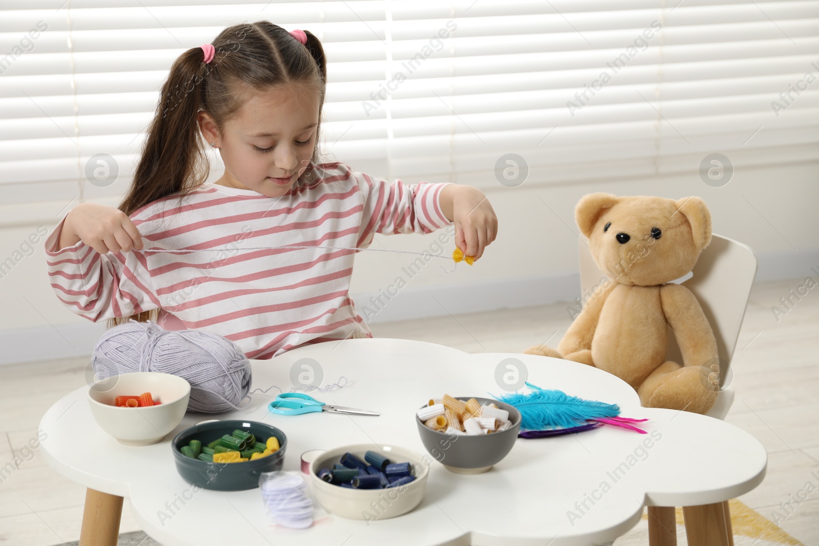 Photo of Little girl making craft at white table indoors. Child creativity and handmade handicraft