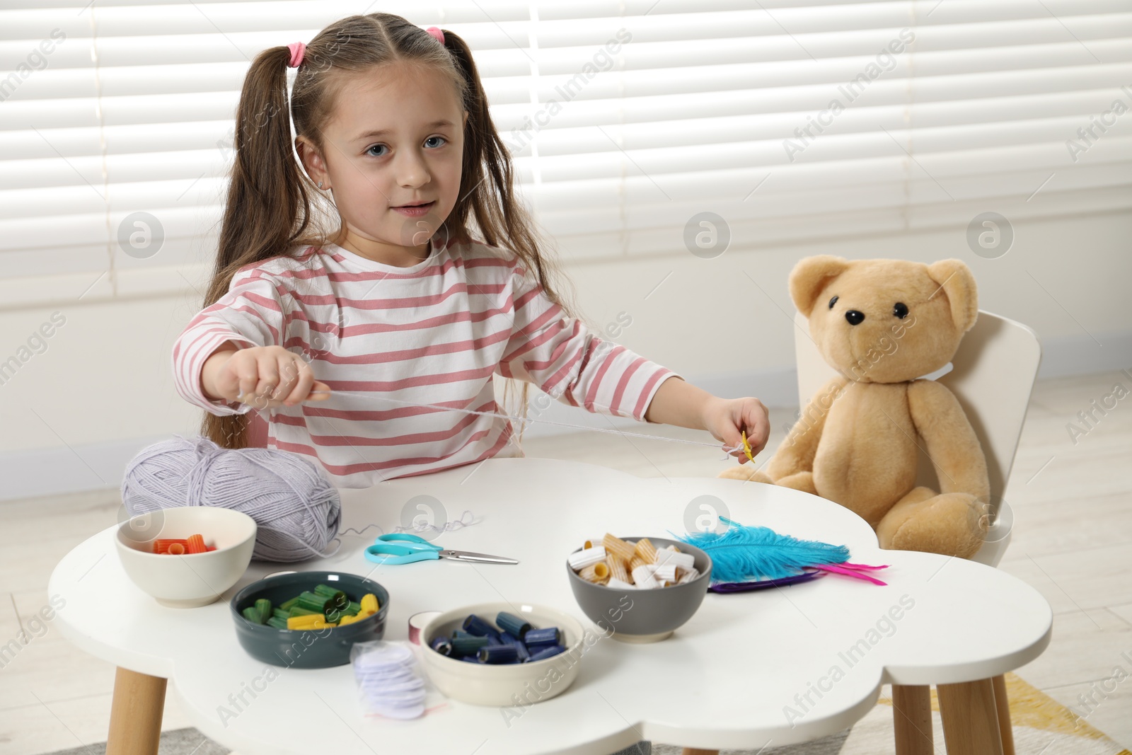 Photo of Little girl making craft at white table indoors. Child creativity and handmade handicraft