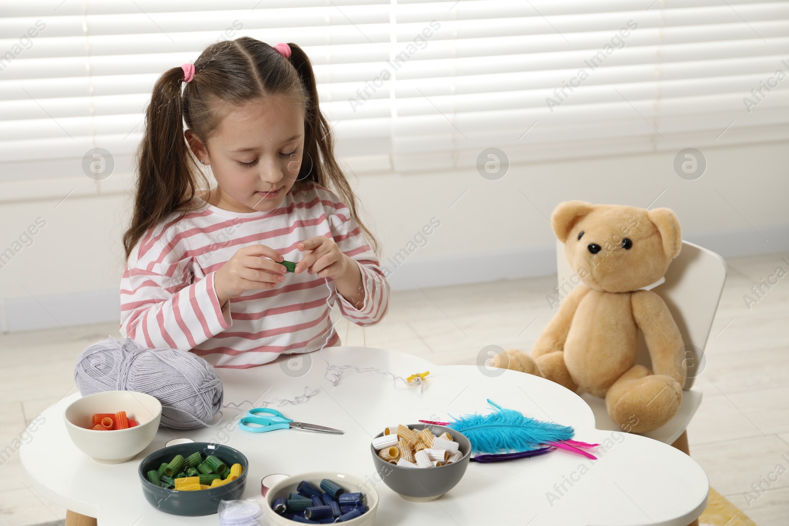 Photo of Little girl making craft at white table indoors. Child creativity and handmade handicraft