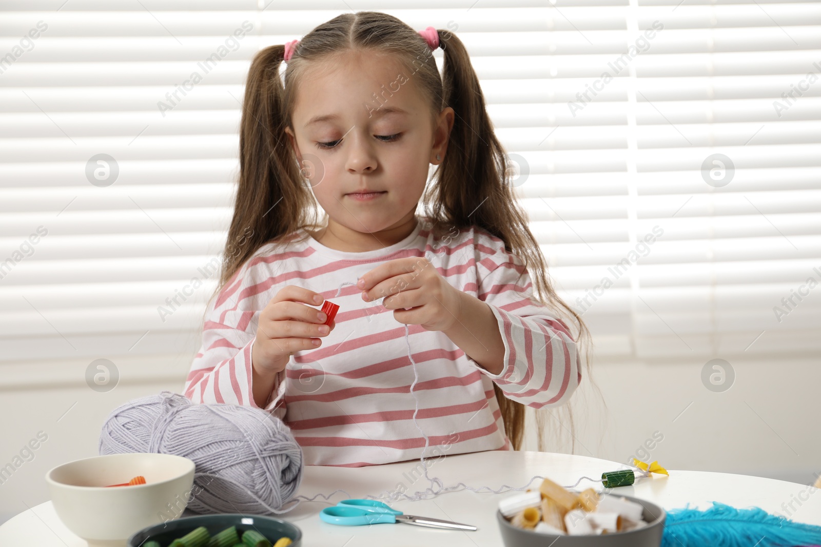 Photo of Little girl making craft at white table indoors. Child creativity and handmade handicraft