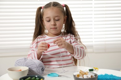 Photo of Little girl making craft at white table indoors. Child creativity and handmade handicraft