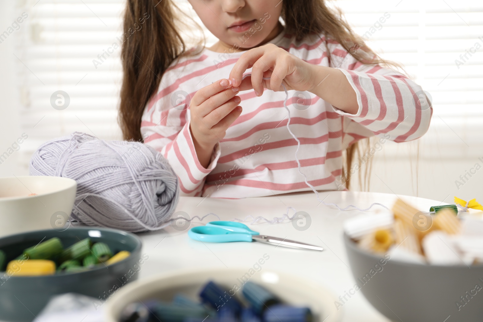 Photo of Little girl making craft at white table indoors, closeup. Child creativity and handmade handicraft