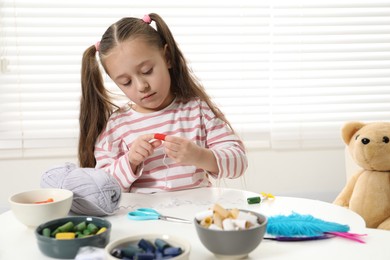 Photo of Little girl making craft at white table indoors. Child creativity and handmade handicraft