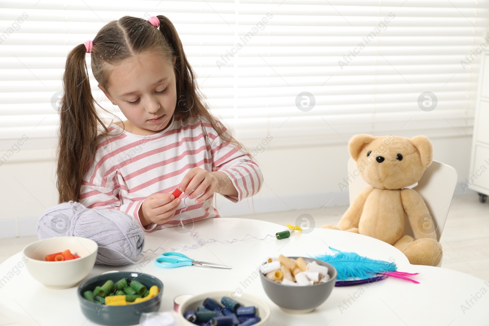 Photo of Little girl making craft at white table indoors. Child creativity and handmade handicraft