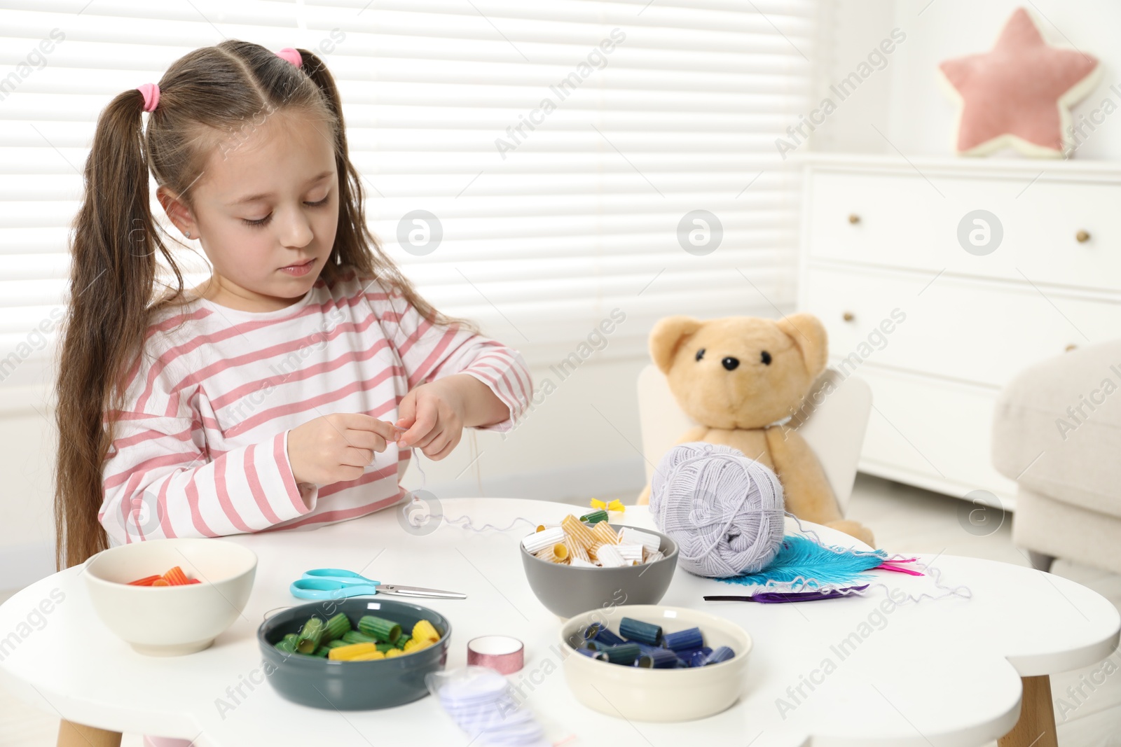 Photo of Little girl making craft at white table indoors. Child creativity and handmade handicraft