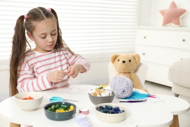 Photo of Little girl making craft at white table indoors. Child creativity and handmade handicraft