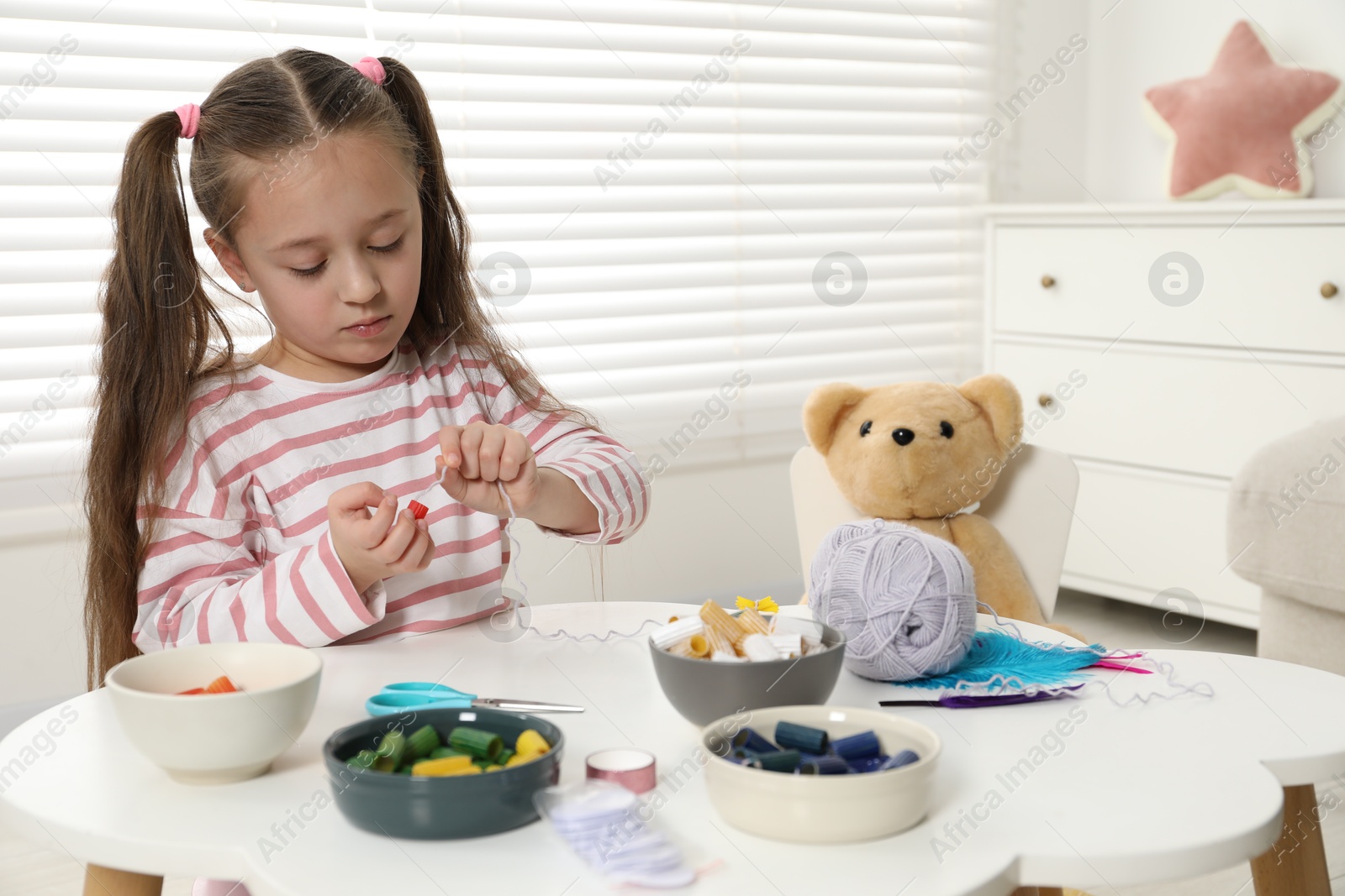 Photo of Little girl making craft at white table indoors. Child creativity and handmade handicraft