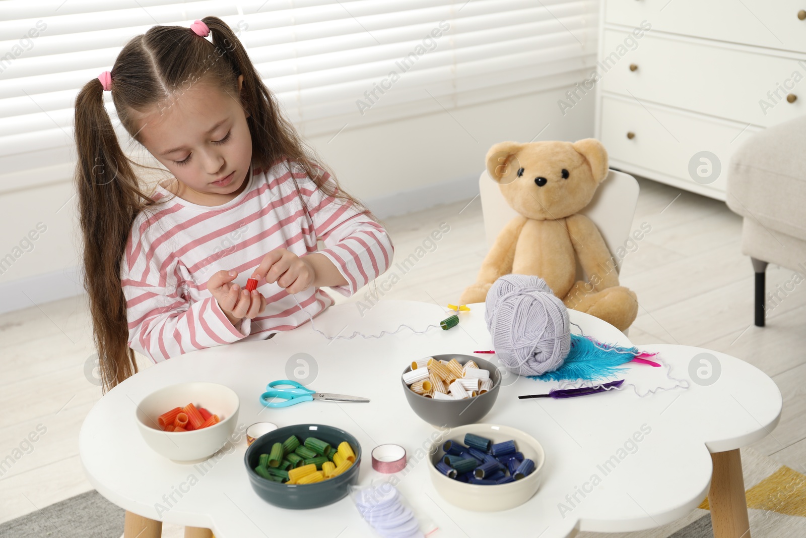 Photo of Little girl making craft at white table indoors. Child creativity and handmade handicraft