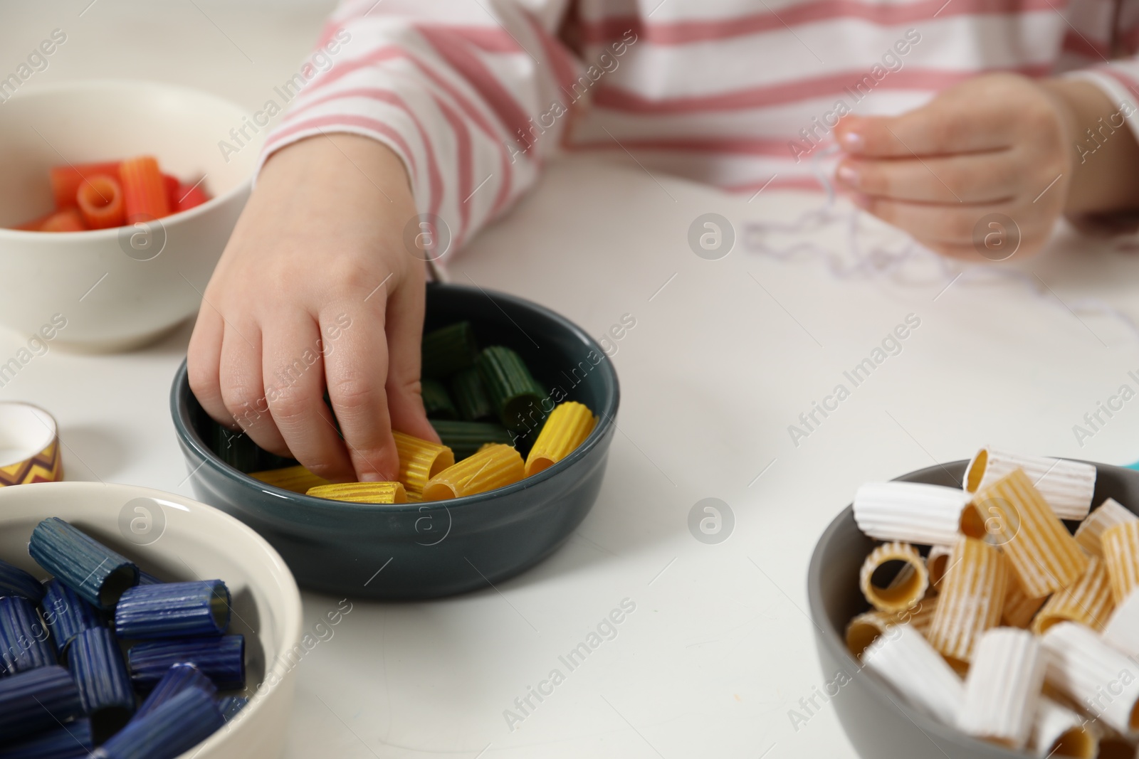 Photo of Little girl making craft at white table, closeup. Child creativity and handmade handicraft