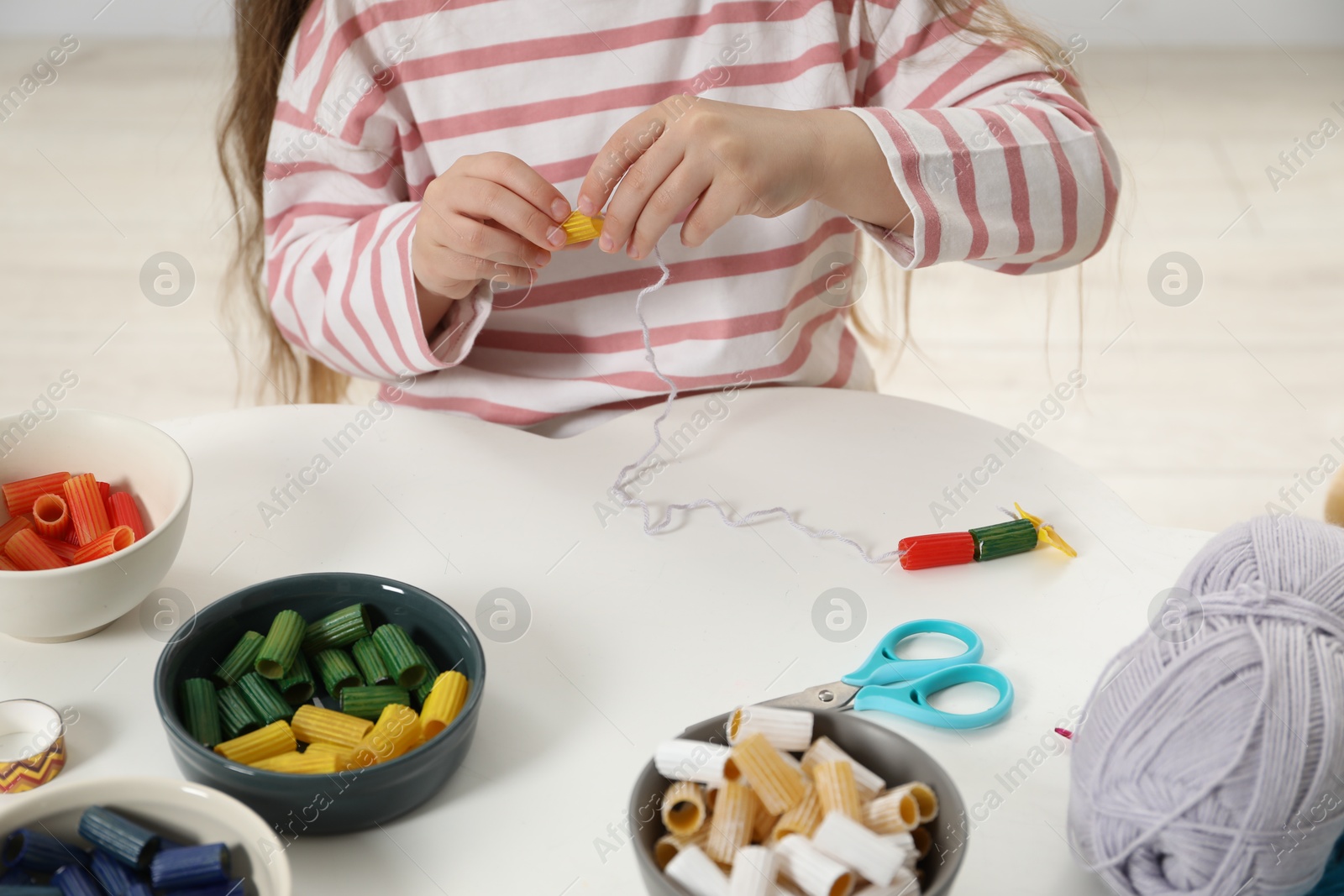 Photo of Little girl making craft at white table indoors, closeup. Child creativity and handmade handicraft