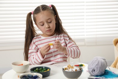 Photo of Little girl making craft at white table indoors. Child creativity and handmade handicraft