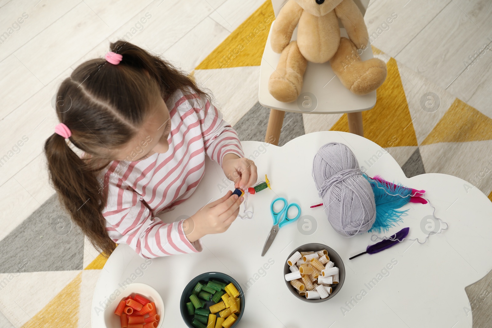 Photo of Little girl making craft at white table indoors, top view. Child creativity and handmade handicraft