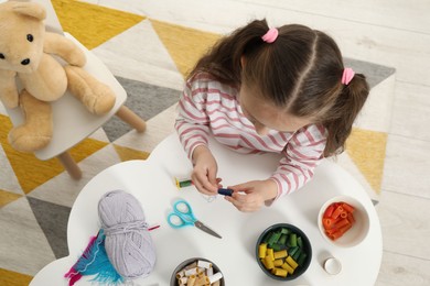 Photo of Little girl making craft at white table indoors, top view. Child creativity and handmade handicraft