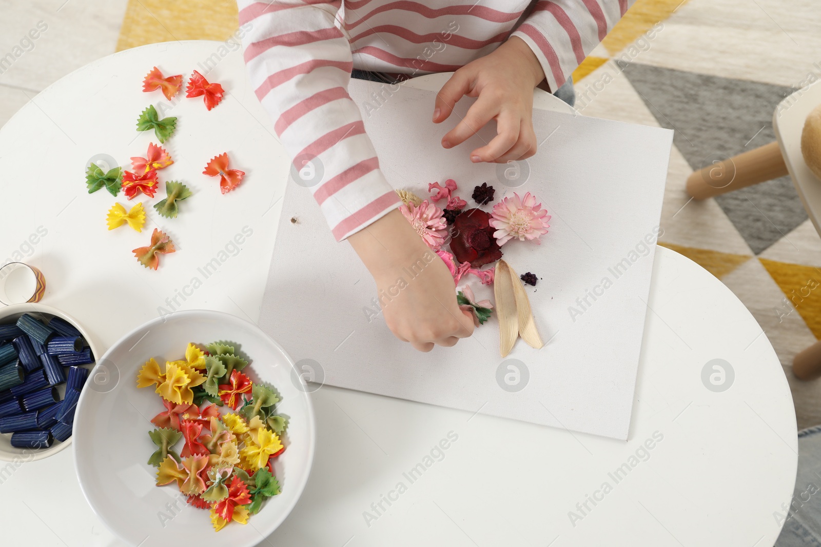 Photo of Little girl making craft at white table indoors, top view. Child creativity and handmade handicraft