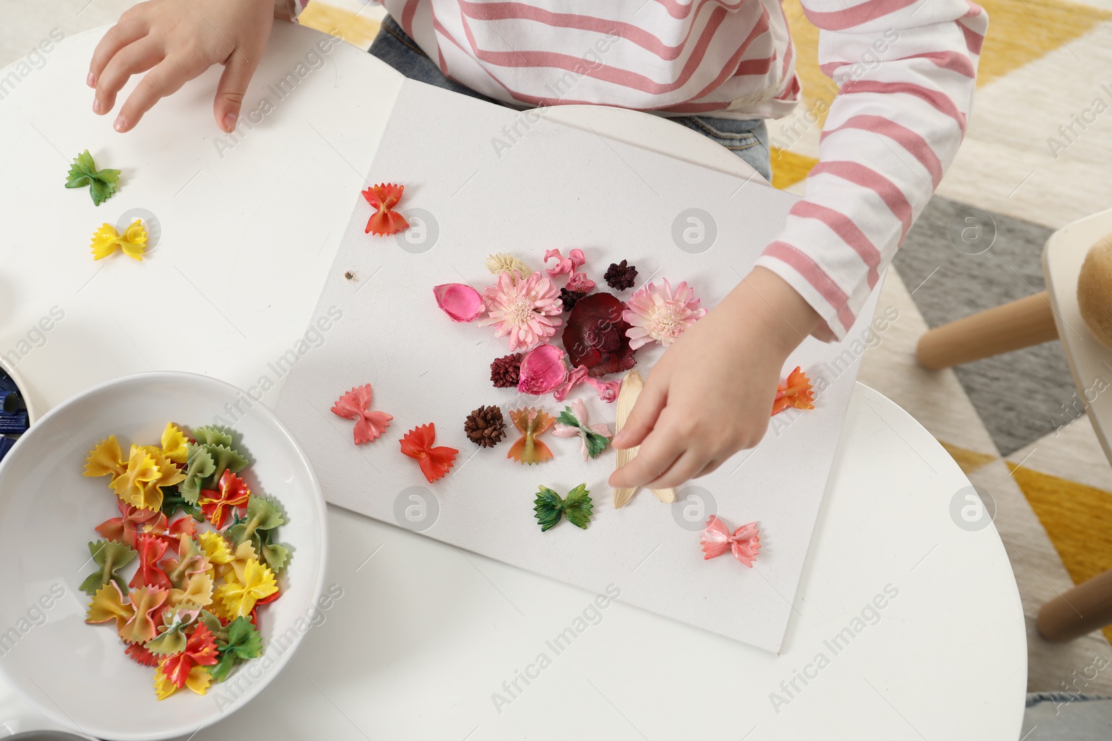 Photo of Little girl making craft at white table indoors, top view. Child creativity and handmade handicraft