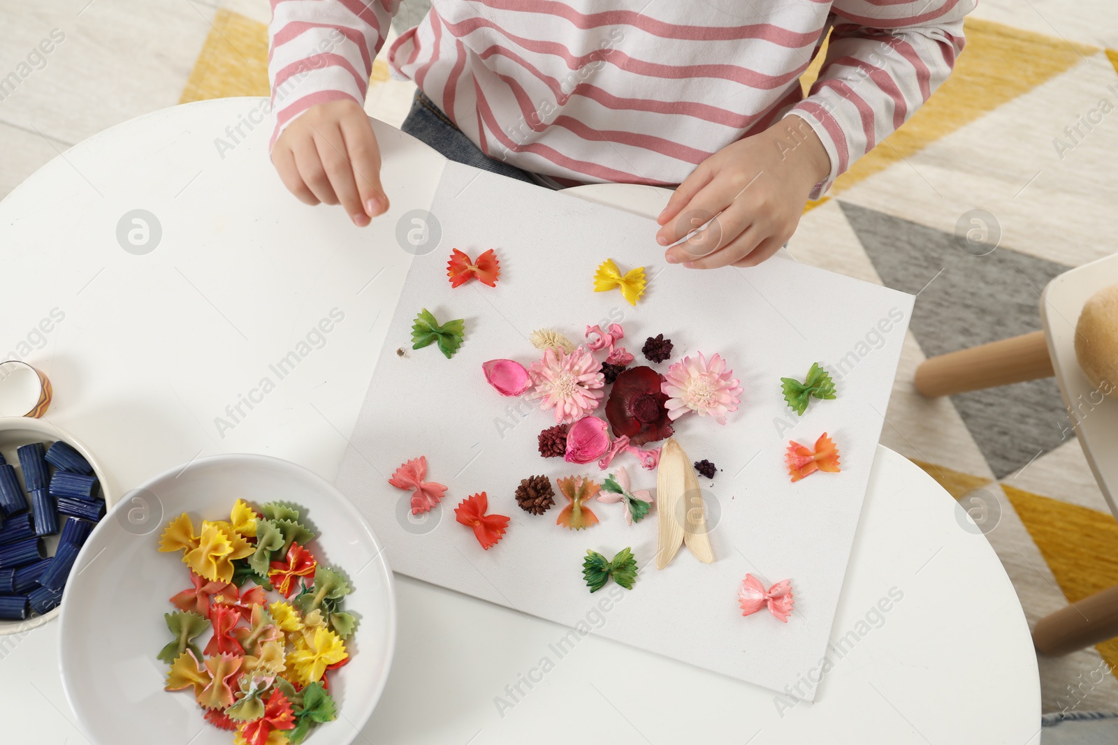 Photo of Little girl making craft at white table indoors, top view. Child creativity and handmade handicraft