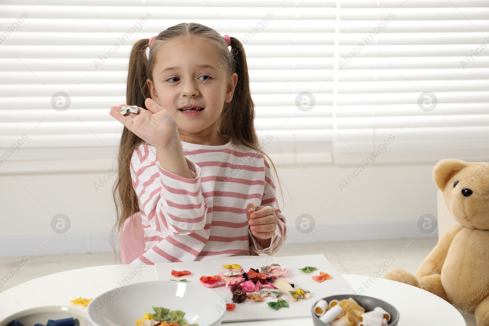 Photo of Little girl making craft at white table indoors. Child creativity and handmade handicraft