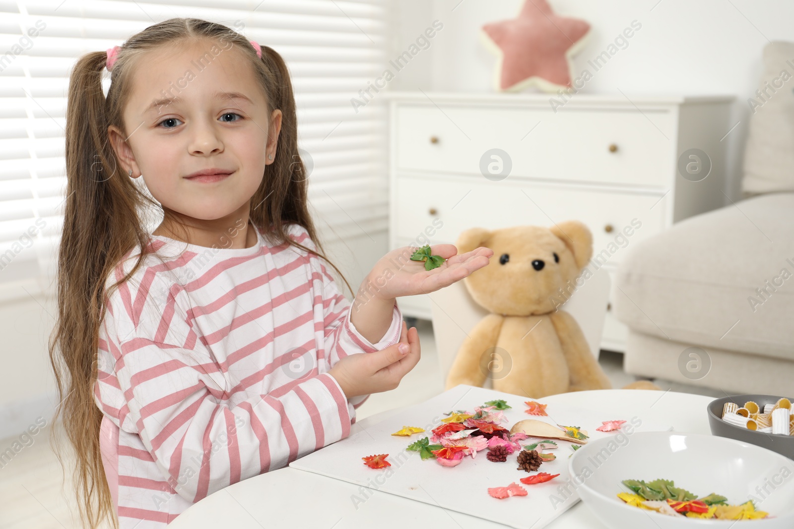 Photo of Little girl making craft at white table indoors. Child creativity and handmade handicraft