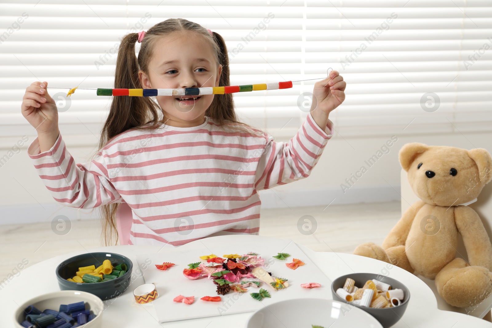 Photo of Little girl with handmade necklace at home. Child creativity and craft