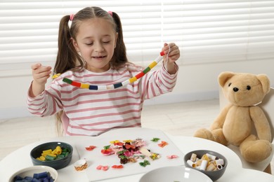 Photo of Little girl with handmade necklace at home. Child creativity and craft