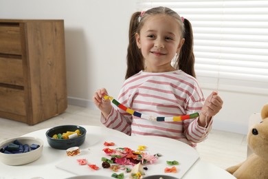 Photo of Little girl with handmade necklace at home. Child creativity and craft