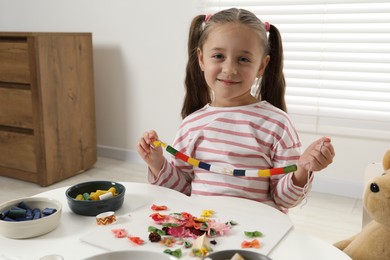 Photo of Little girl with handmade necklace at home. Child creativity and craft