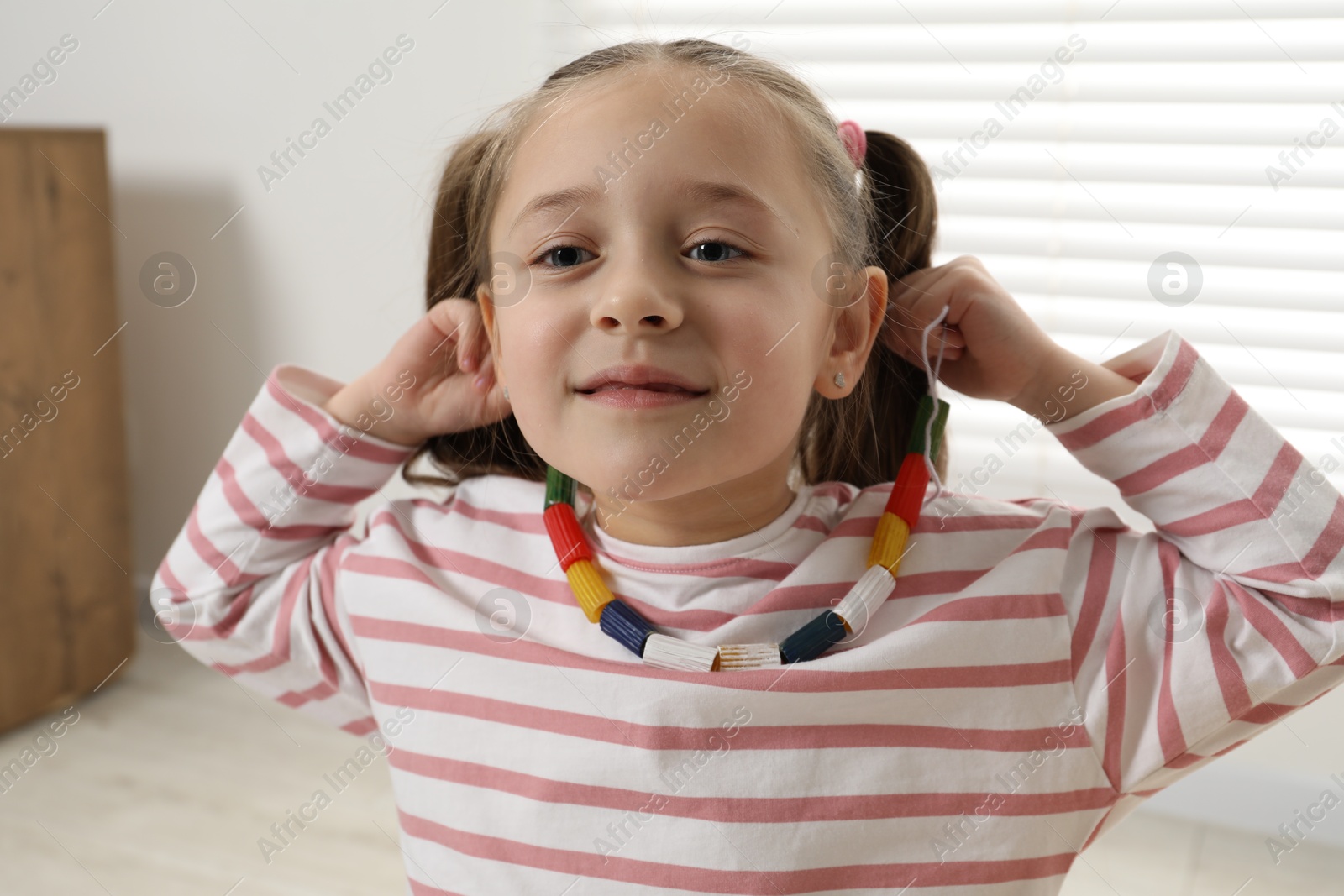 Photo of Little girl with handmade necklace at home. Child creativity and craft