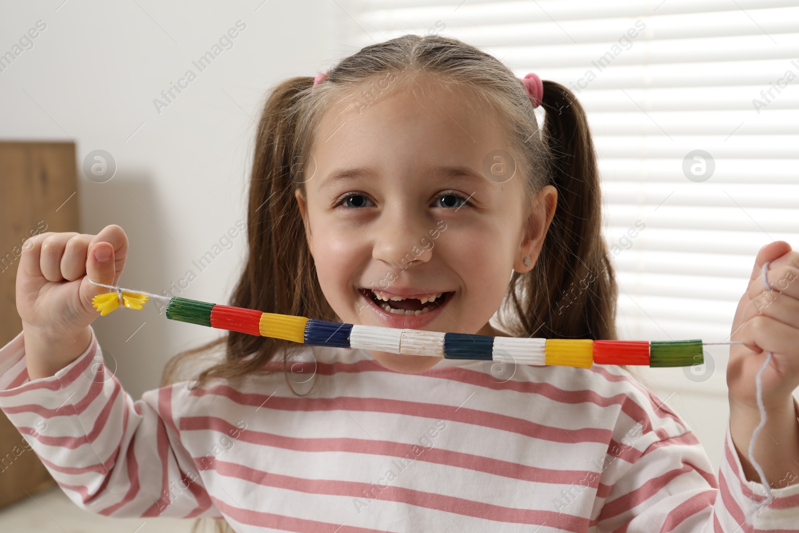 Photo of Little girl with handmade necklace at home. Child creativity and craft