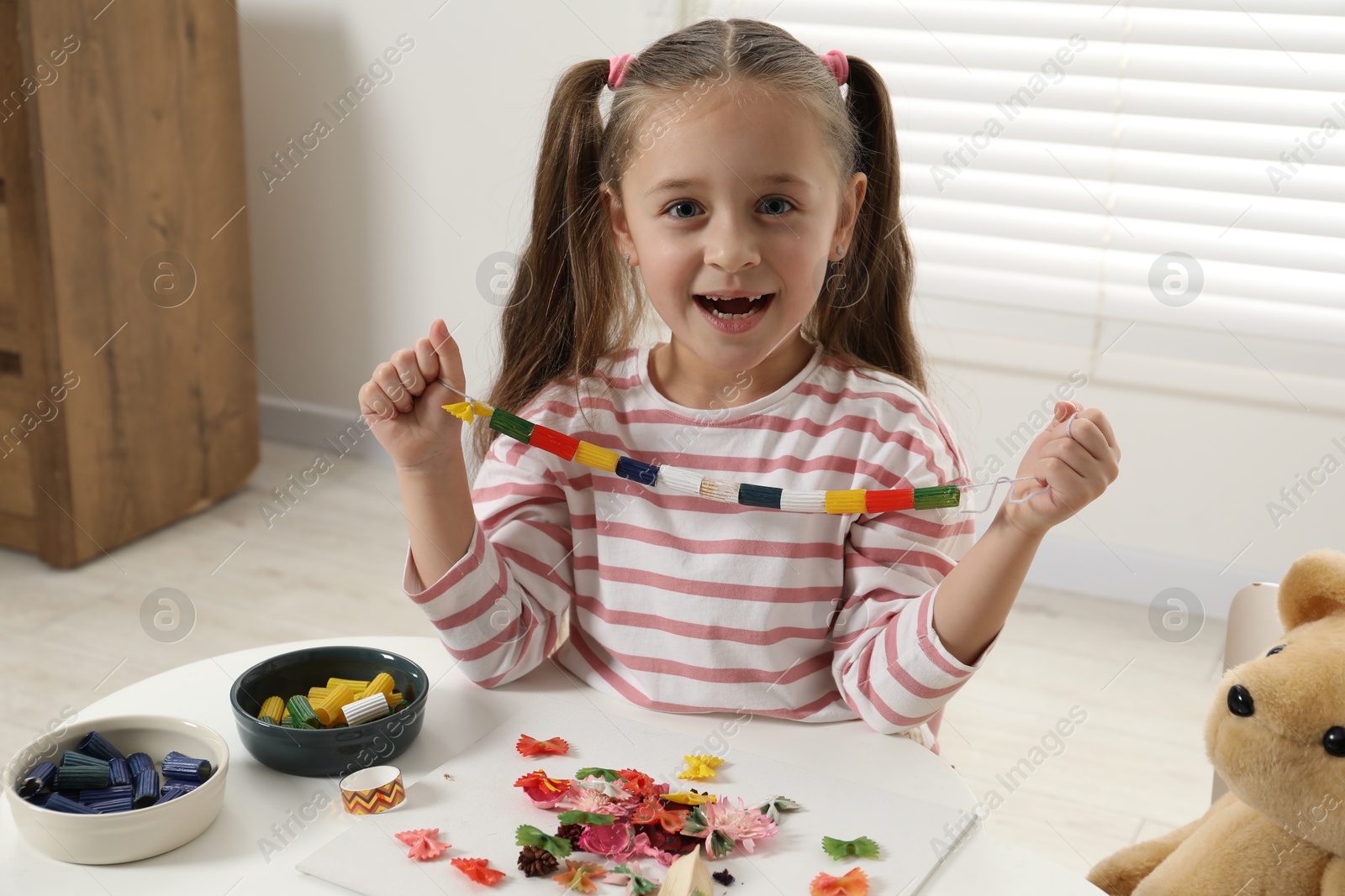 Photo of Little girl with handmade necklace at home. Child creativity and craft