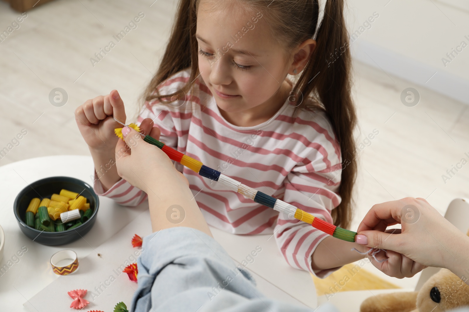 Photo of Woman and little girl making craft at white table indoors. Child creativity